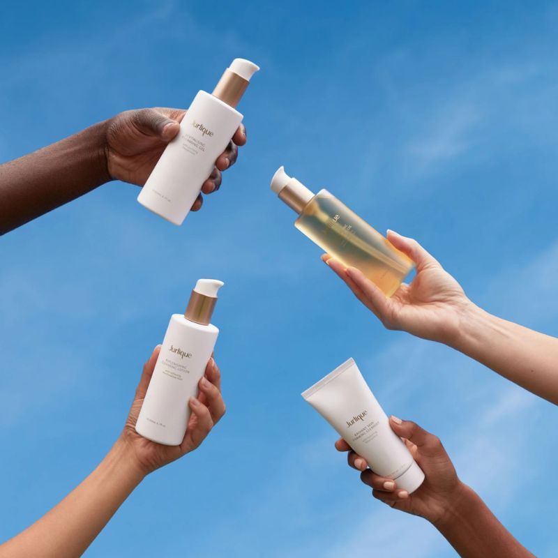 Hands holding various skincare products against a blue sky