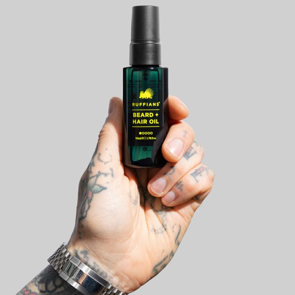 Hand holding a bottle of Ruffians beard and hair oil against a gray background